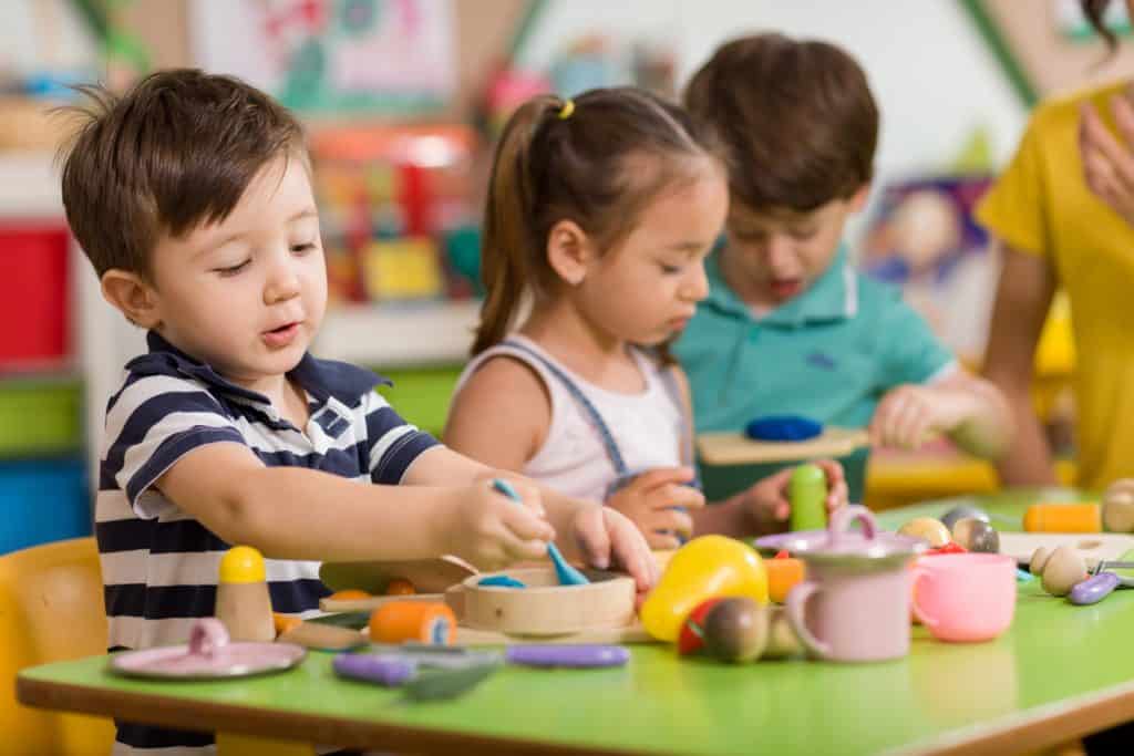 Three preschool students playing with clay in a classroom.