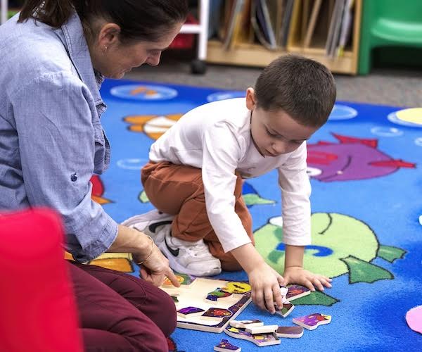 Ms. Noreen works with a student on a puzzle on the floor.