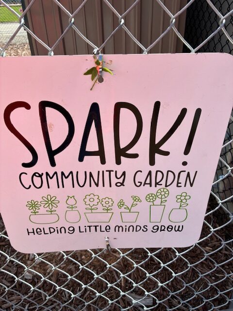 Sign for a community garden titled "SPARK!" with images of plants, stating "Helping little minds grow."