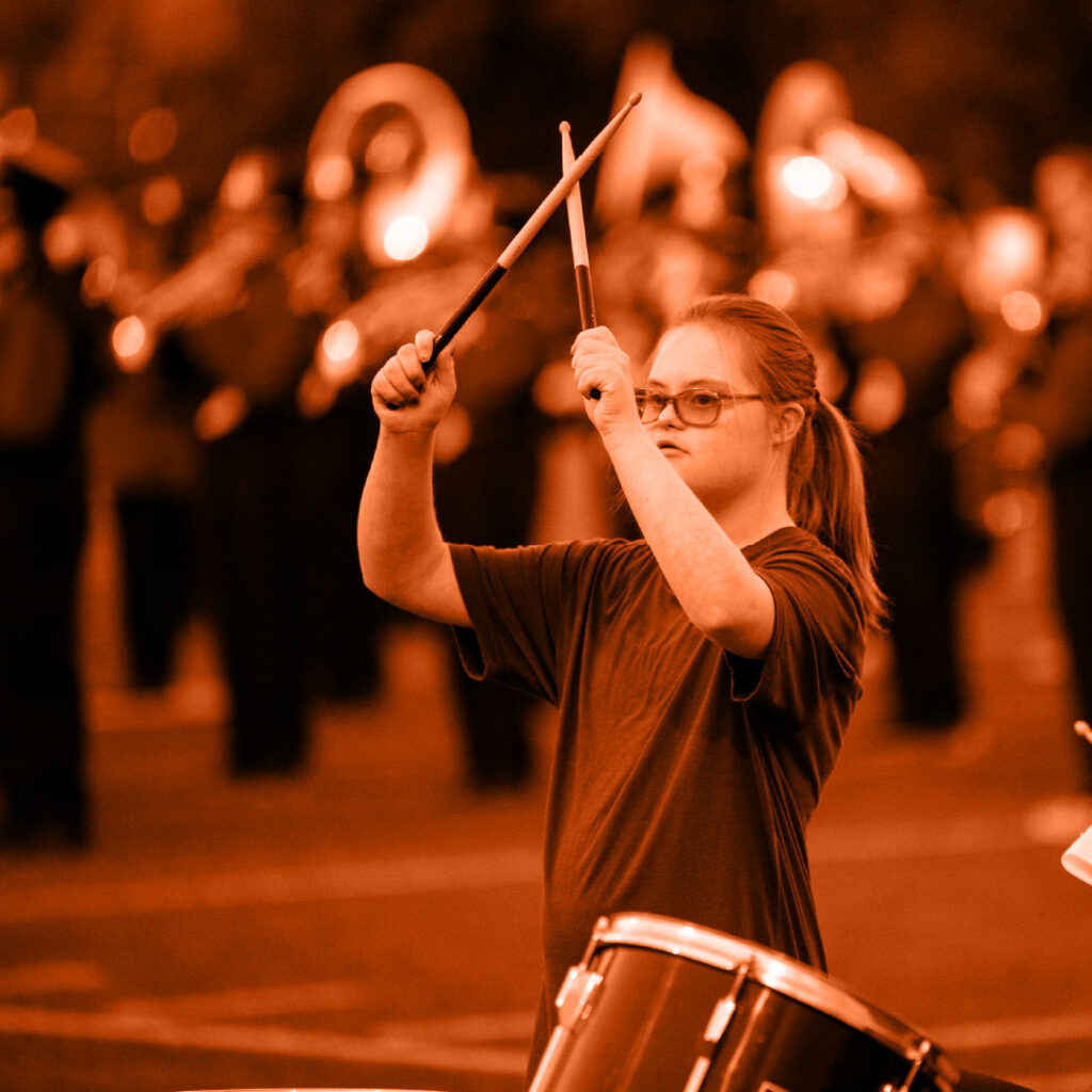 Female band member crossing her drum sticks and playing her drum.