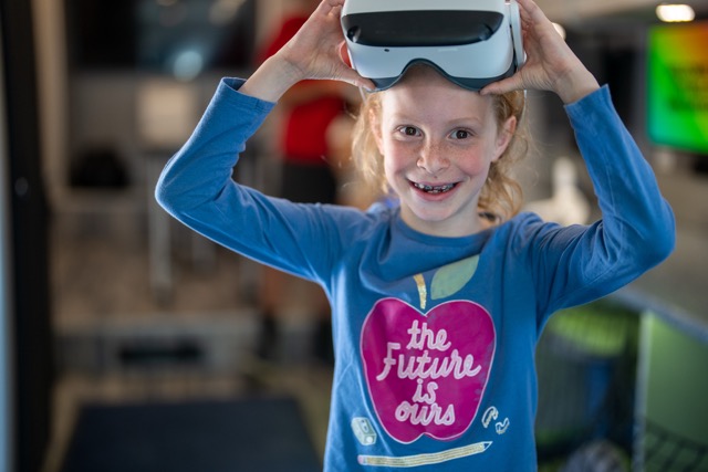 A red haired girl wearing a shirt that says "The Future is Ours" She is wearing a VR headset.